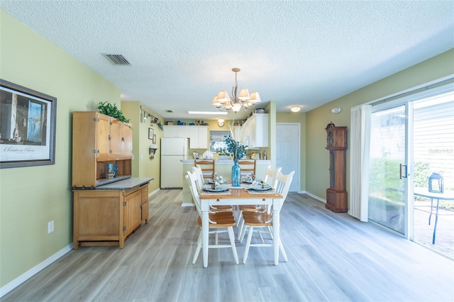 dining area with a textured ceiling, a notable chandelier, visible vents, and light wood-type flooring