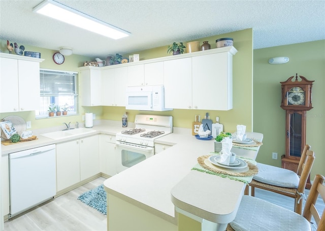 kitchen featuring white appliances, light countertops, a peninsula, and a sink