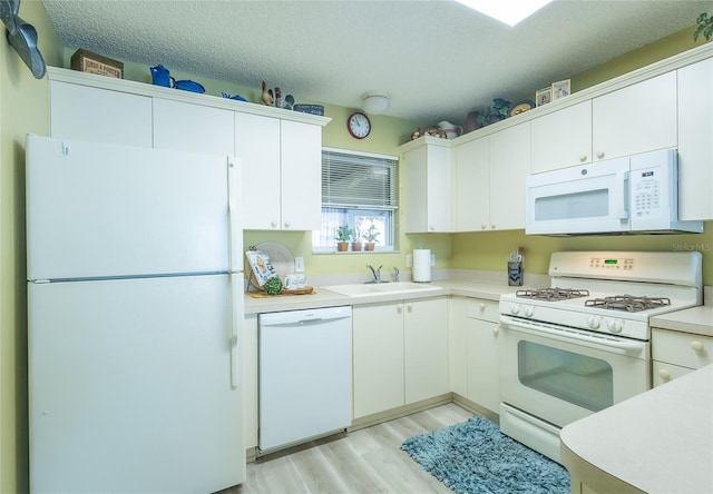 kitchen featuring white appliances, light wood finished floors, a sink, light countertops, and a textured ceiling