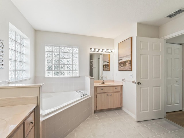 bathroom featuring tiled tub, vanity, and tile patterned floors