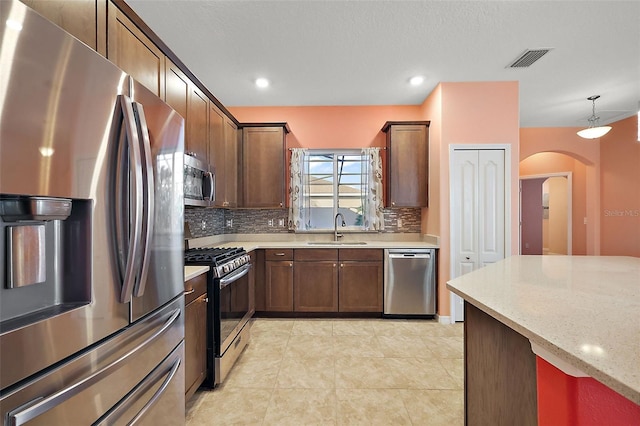 kitchen with sink, hanging light fixtures, stainless steel appliances, light stone counters, and decorative backsplash