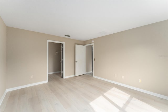 unfurnished bedroom featuring a spacious closet, light hardwood / wood-style floors, and a closet