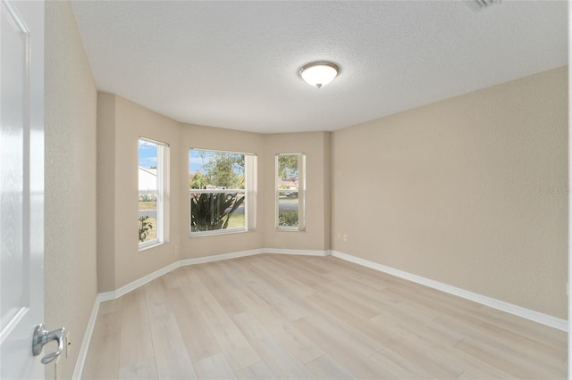 spare room featuring a textured ceiling and light hardwood / wood-style floors