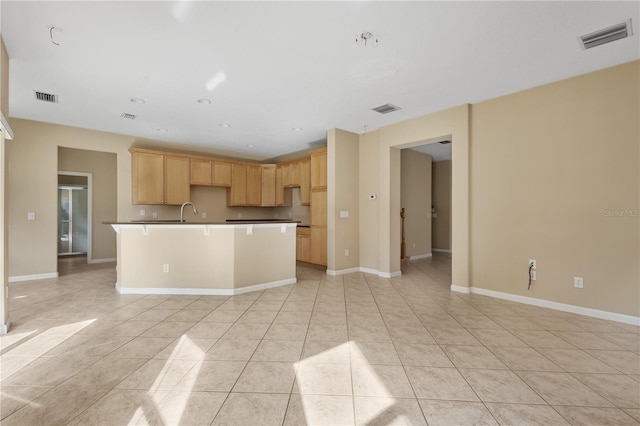 kitchen with light tile patterned flooring, sink, a kitchen island with sink, and light brown cabinets