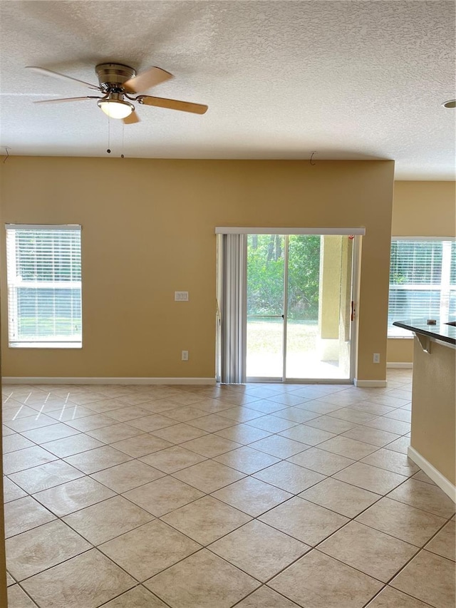 spare room with baseboards, light tile patterned floors, ceiling fan, and a textured ceiling