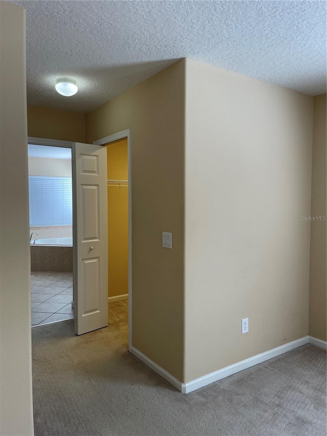 spare room with a textured ceiling, carpet floors, and baseboards