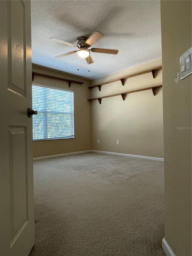 carpeted spare room with a textured ceiling, ceiling fan, and baseboards