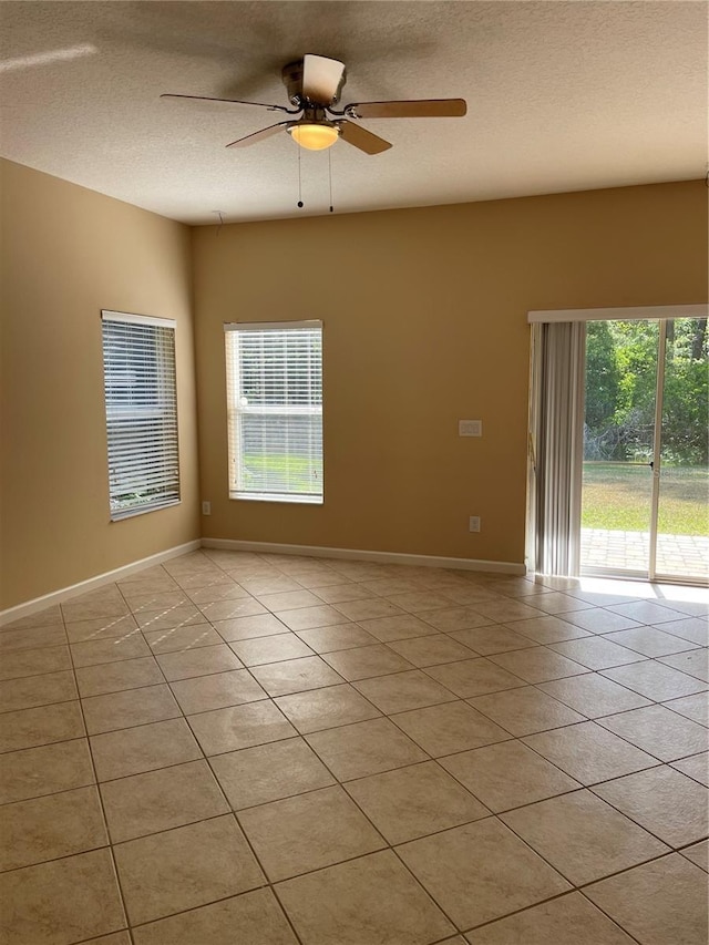 spare room with light tile patterned floors, ceiling fan, baseboards, and a textured ceiling