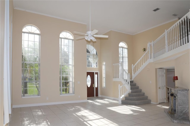 entrance foyer with a high ceiling, ornamental molding, light tile patterned floors, and ceiling fan