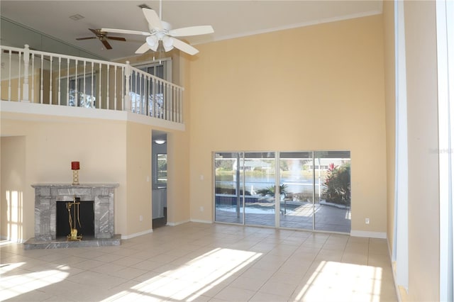 unfurnished living room with light tile patterned flooring, crown molding, a towering ceiling, ceiling fan, and a fireplace