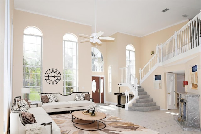 tiled living room with crown molding, a towering ceiling, a premium fireplace, and ceiling fan