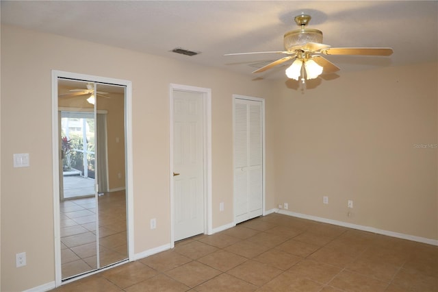 unfurnished bedroom with multiple closets, light tile patterned floors, and ceiling fan