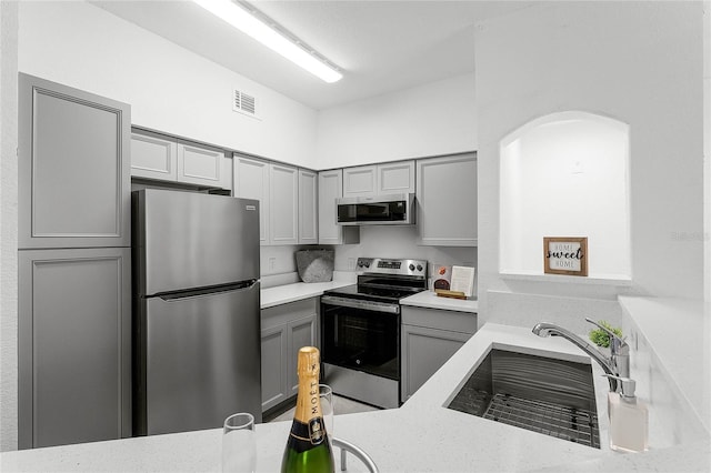 kitchen with gray cabinetry, sink, light stone counters, and stainless steel appliances