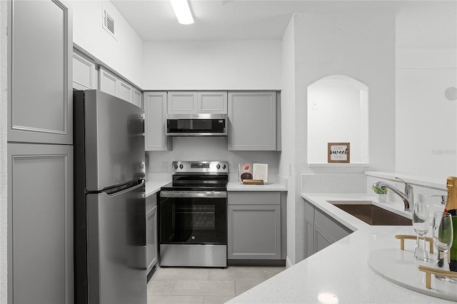 kitchen with gray cabinets, light tile patterned flooring, appliances with stainless steel finishes, sink, and light stone counters