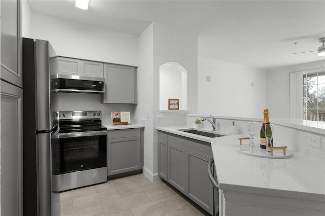 kitchen with appliances with stainless steel finishes, sink, gray cabinetry, ceiling fan, and light stone countertops