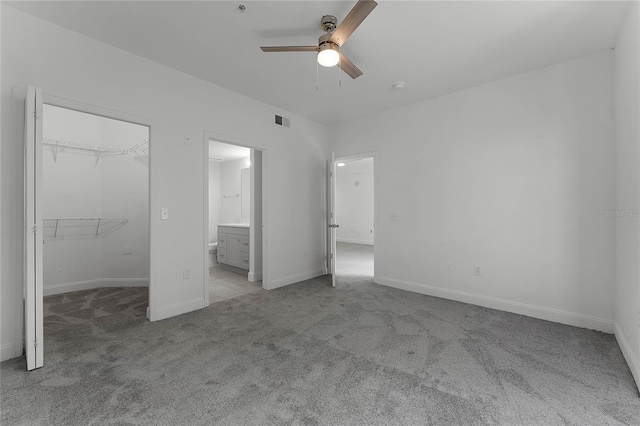 unfurnished bedroom featuring ceiling fan, connected bathroom, light carpet, a spacious closet, and a closet