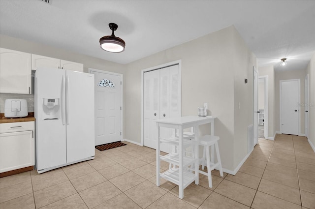 kitchen with butcher block countertops, light tile patterned floors, white fridge with ice dispenser, decorative backsplash, and white cabinets