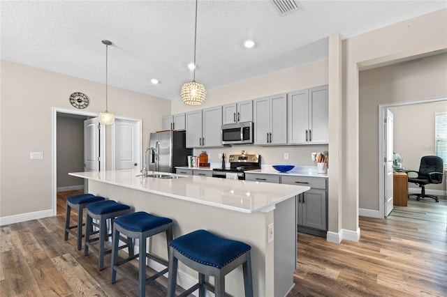 kitchen featuring appliances with stainless steel finishes, decorative light fixtures, an island with sink, and gray cabinetry