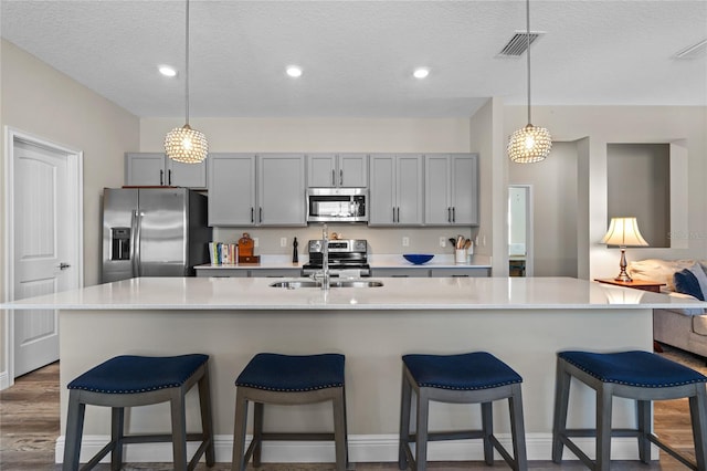 kitchen featuring gray cabinetry, decorative light fixtures, a large island with sink, and appliances with stainless steel finishes