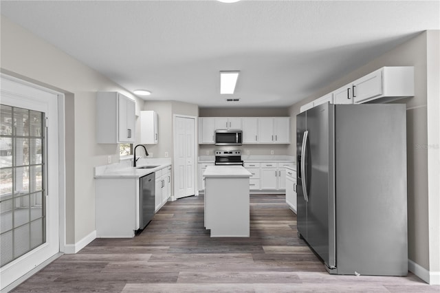 kitchen featuring sink, hardwood / wood-style floors, stainless steel appliances, a center island, and white cabinets