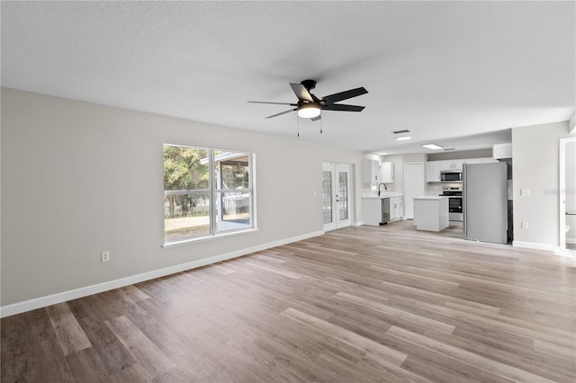 unfurnished living room featuring ceiling fan, a textured ceiling, and light wood-type flooring