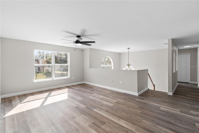 empty room with dark wood-type flooring and ceiling fan with notable chandelier