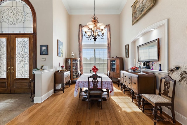 dining space featuring a chandelier, a high ceiling, ornamental molding, light wood-type flooring, and french doors