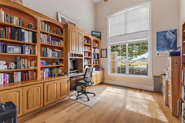 home office featuring a high ceiling, built in desk, and light hardwood / wood-style floors