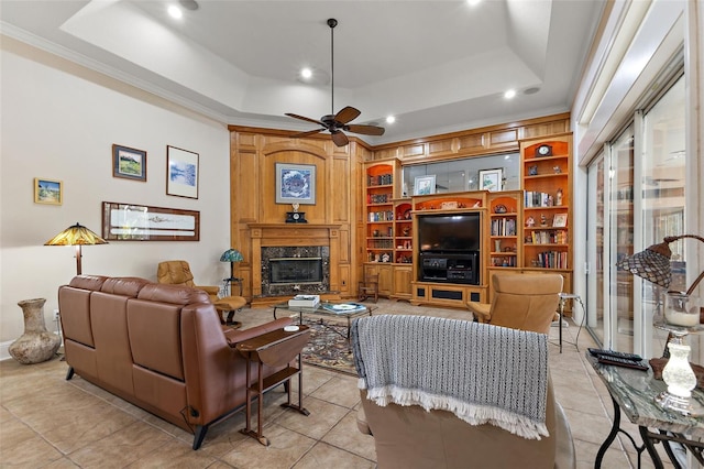 living room with built in shelves, crown molding, a tray ceiling, ceiling fan, and a fireplace