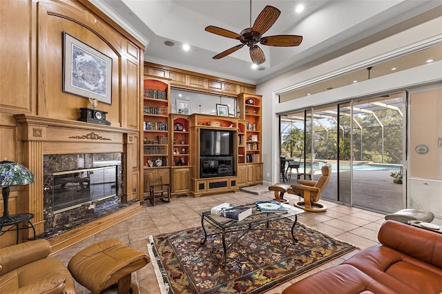 tiled living room with built in shelves, ceiling fan, a high end fireplace, and ornamental molding