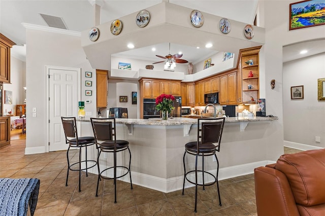 kitchen featuring a kitchen bar, kitchen peninsula, ceiling fan, light stone countertops, and black appliances