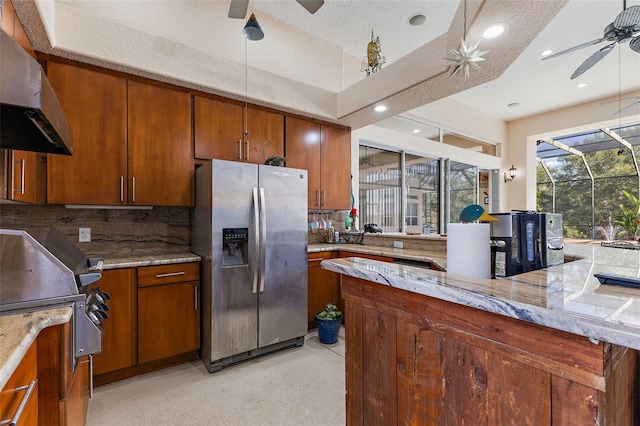 kitchen featuring ceiling fan, backsplash, light stone counters, stainless steel fridge with ice dispenser, and wall chimney exhaust hood