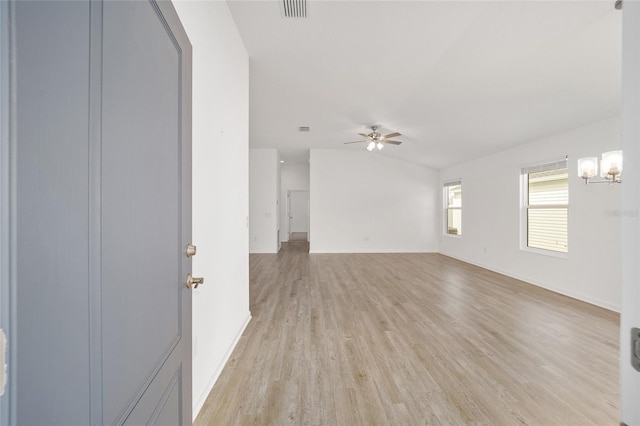 empty room featuring vaulted ceiling, ceiling fan with notable chandelier, and light wood-type flooring