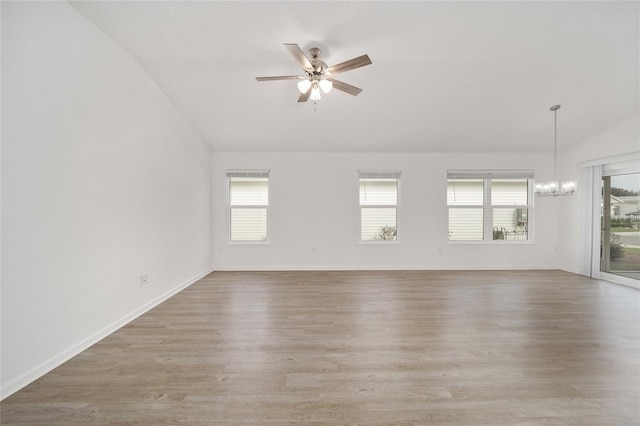 spare room featuring ceiling fan with notable chandelier, vaulted ceiling, and wood-type flooring