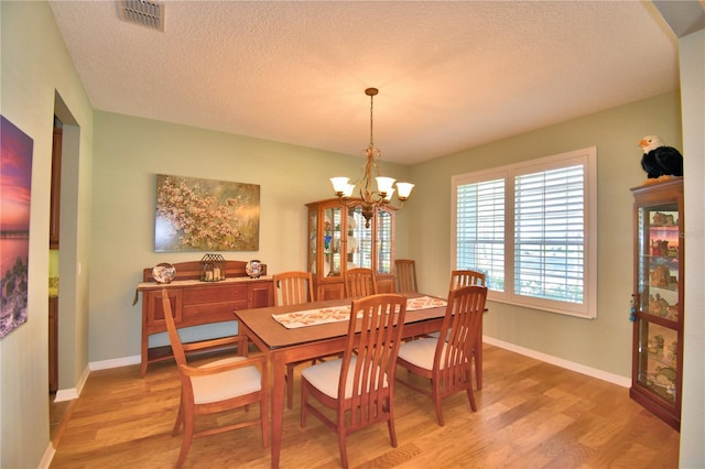 dining area featuring a textured ceiling, a notable chandelier, and light hardwood / wood-style floors