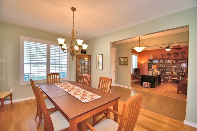 dining area with ceiling fan with notable chandelier, wood-type flooring, and a textured ceiling