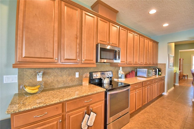 kitchen with tasteful backsplash, light stone countertops, a textured ceiling, and appliances with stainless steel finishes