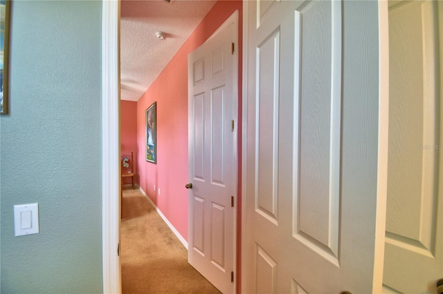 hallway featuring light carpet and a textured ceiling