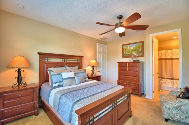 bedroom with ceiling fan, light carpet, ensuite bathroom, and a textured ceiling