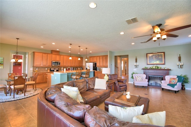 living room with ceiling fan, sink, a textured ceiling, and light tile patterned floors