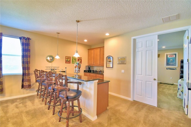 kitchen featuring decorative light fixtures, light carpet, a breakfast bar area, and a textured ceiling