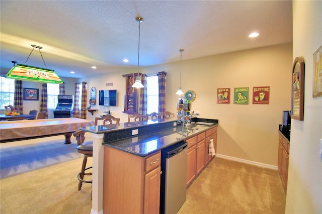 kitchen with a breakfast bar area, dark stone counters, stainless steel dishwasher, light colored carpet, and kitchen peninsula