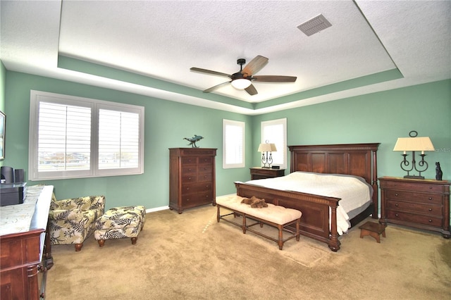 carpeted bedroom with ceiling fan, a tray ceiling, and a textured ceiling