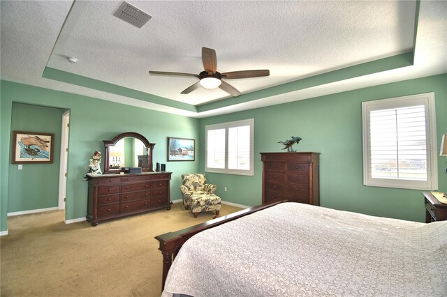 bedroom featuring light carpet, a raised ceiling, and a textured ceiling