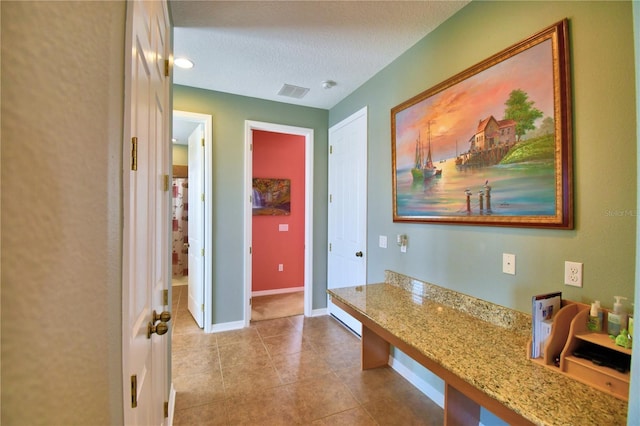 hallway with a textured ceiling and light tile patterned flooring