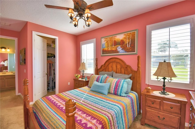 carpeted bedroom featuring ceiling fan, connected bathroom, a textured ceiling, a walk in closet, and a closet