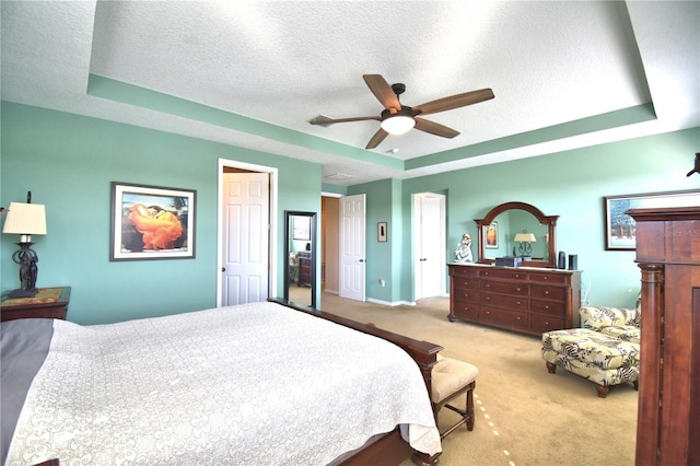 bedroom featuring ceiling fan, light colored carpet, a tray ceiling, and a textured ceiling