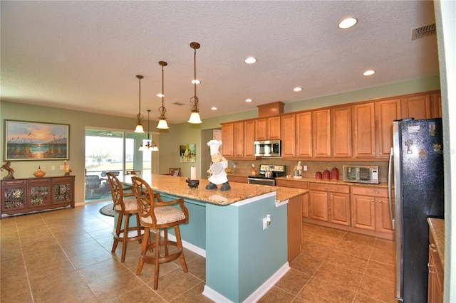 kitchen featuring a kitchen bar, hanging light fixtures, a kitchen island, stainless steel appliances, and decorative backsplash