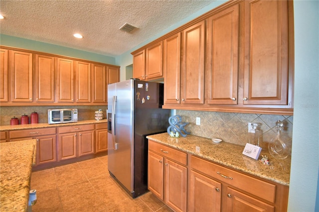 kitchen featuring light tile patterned floors, stainless steel refrigerator with ice dispenser, light stone counters, a textured ceiling, and decorative backsplash