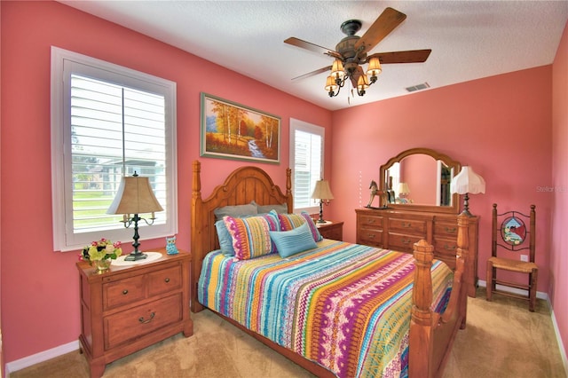 bedroom with ceiling fan, light colored carpet, and a textured ceiling